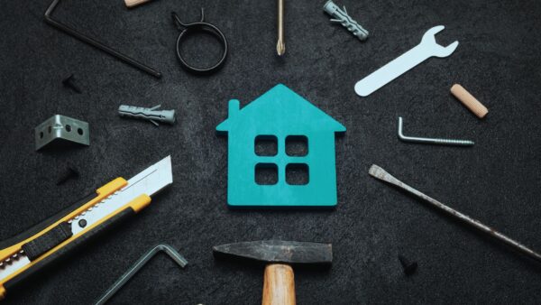 Cut out of blue house laying on gray background surrounded by tools.