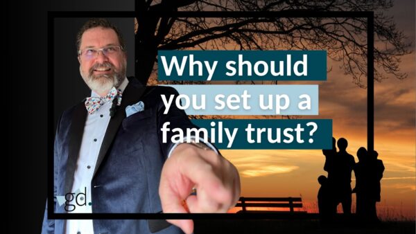 Man in suit jacket and bow tie with beard and glasses pointing at a title "Why should you set up a family trust?" on a photo of a sunset with a family next to a bench.