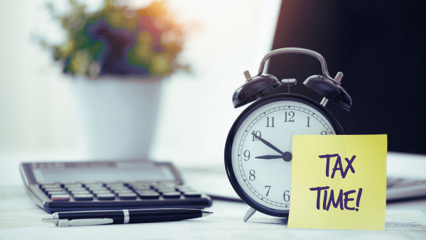 Old fashioned alarm clock on a desk with a calculator and a pen, and computer, and a flower in the background