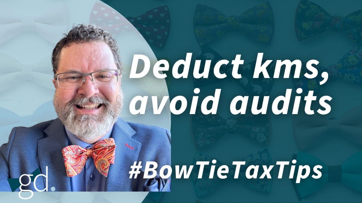 White male, dark curly hair, whitish beard, wearing glasses, a blue suit jacket, blue shirt and orange patterned bow tie talking about "deducting kilometres using a car log"