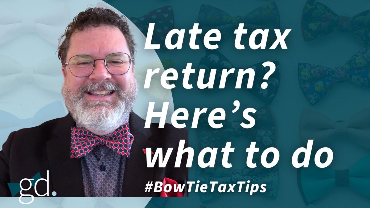 White male with glasses and short curly hair and a white beard wearing a red checked bow tie, dark jacket, and gray dress shirt talking about filing taxes late in Canada