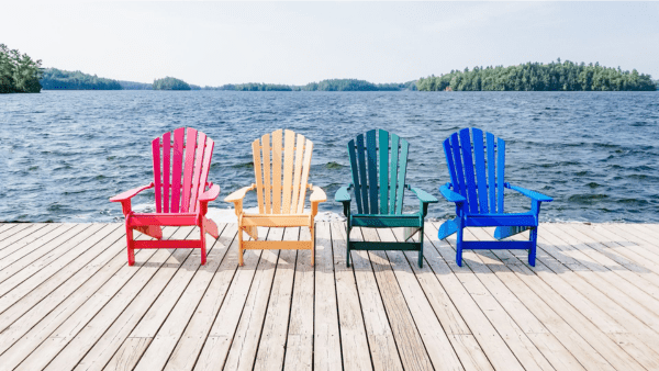 4 muskoka chairs on a dock in front of a lake - red, yellow, green, and blue