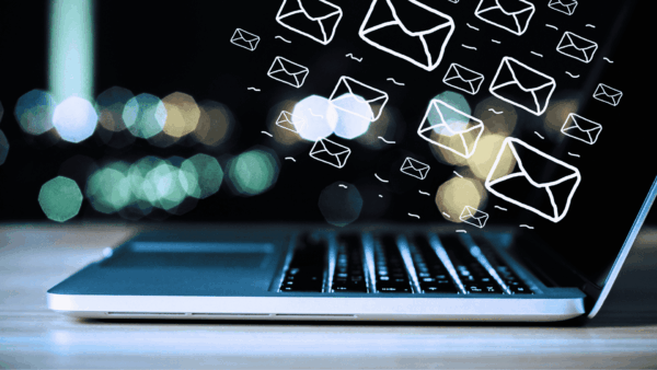 Laptop on gray desk with dark background and light spots, with little email icons flying out of the screen